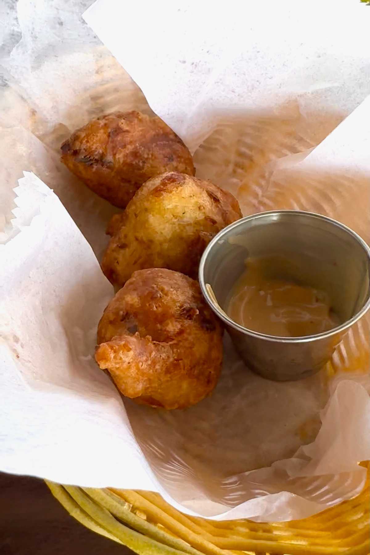 Basket with 3 fishcakes and a ramekin with sauce.